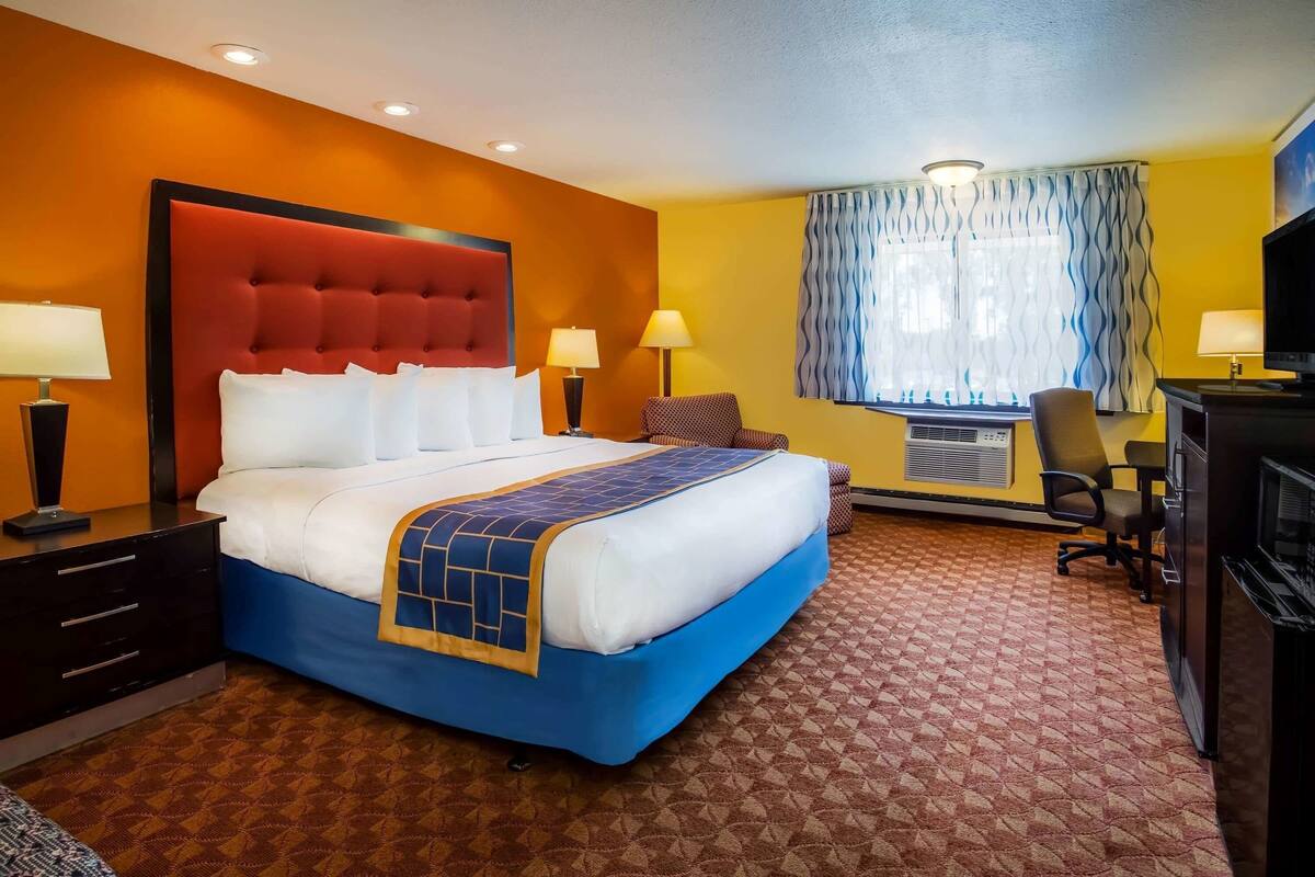 Habitación de hotel con una cama grande, dos mesitas de noche, un escritorio con silla, un televisor y una ventana con cortinas.