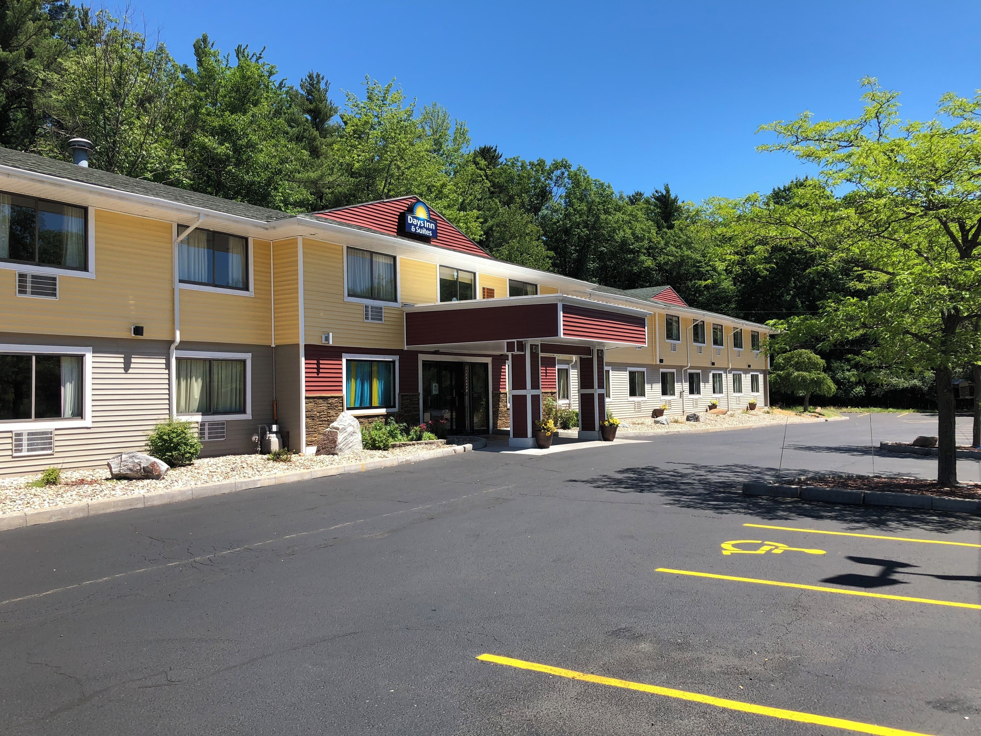 Un motel de varios pisos con un letrero de Days Inn & Suites, un acceso cubierto y un estacionamiento con espacios para discapacitados.