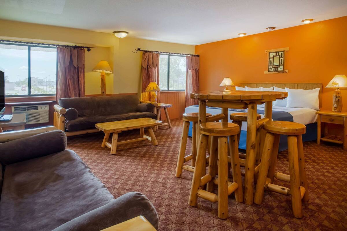 Habitación de hotel con sofá, una mesita, taburetes de madera, cama y ventana con cortinas.