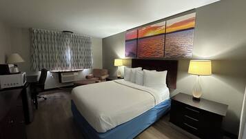 A hotel room with a bed, two bedside lamps, a desk with a lamp, a chair, and a wall-mounted TV.