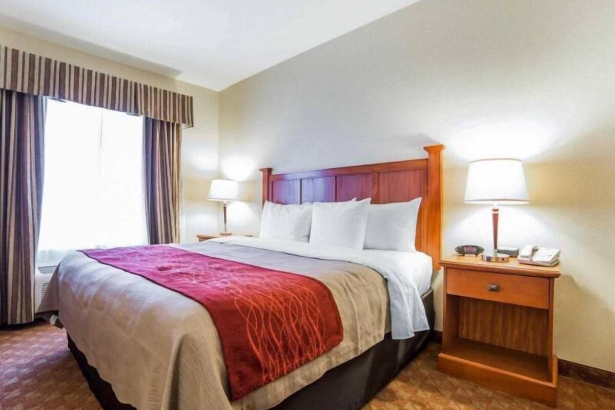 A hotel room with a bed, two bedside tables, a lamp, a phone, and a window with curtains.