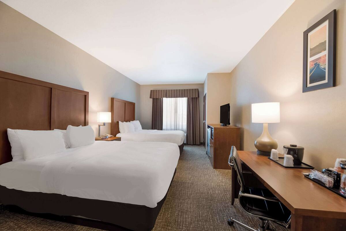 A hotel room with two beds, a desk, a chair, a TV, and a window with curtains.