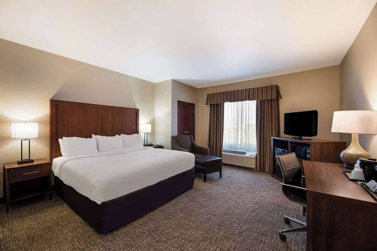 A hotel room with a large bed, a desk with a computer, a chair, a TV, and a window with curtains.