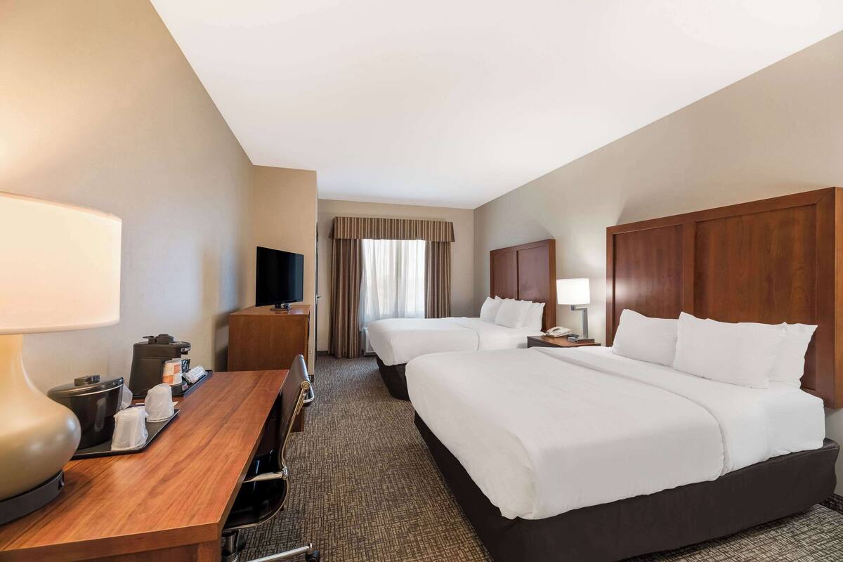 A hotel room with two beds, a desk with a lamp, a television, and a window with curtains.