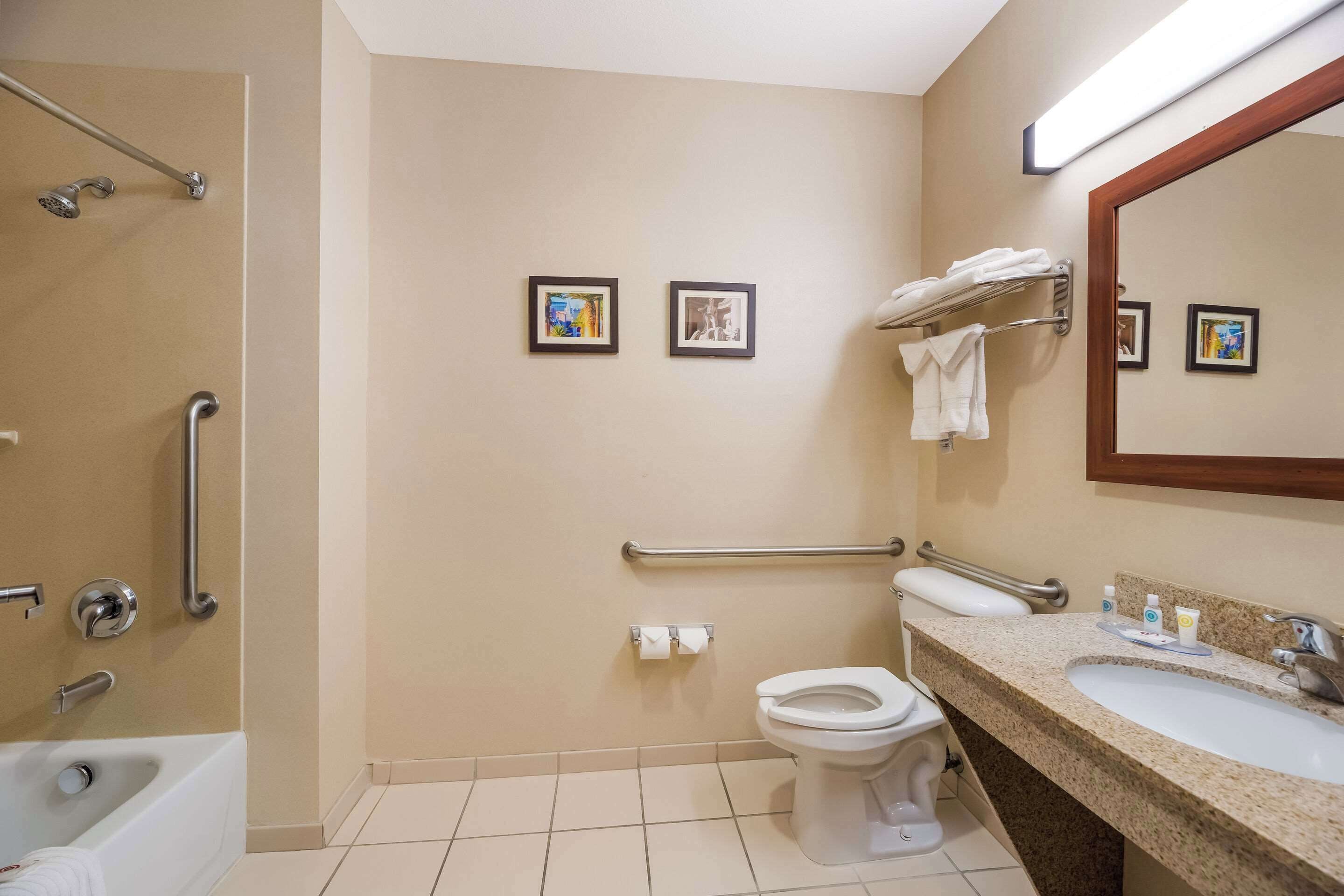 A bathroom with a bathtub, toilet, and sink, equipped with handrails and a mirror.