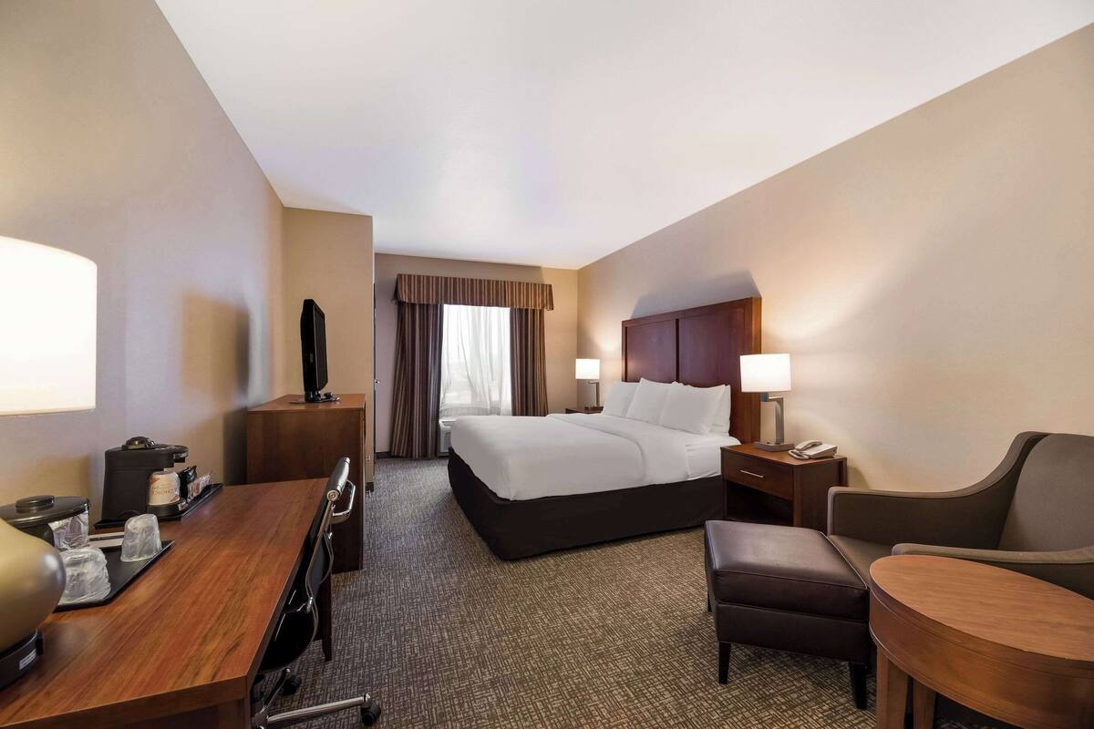 A hotel room with a bed, a desk with a computer, a chair, a small table, and a TV.