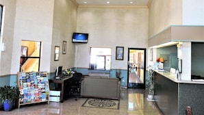 A lobby with a reception desk, a flat-screen TV mounted on the wall, a seating area with a sofa, and a display rack with brochures. - Mission Inn and Suites (Hayward)