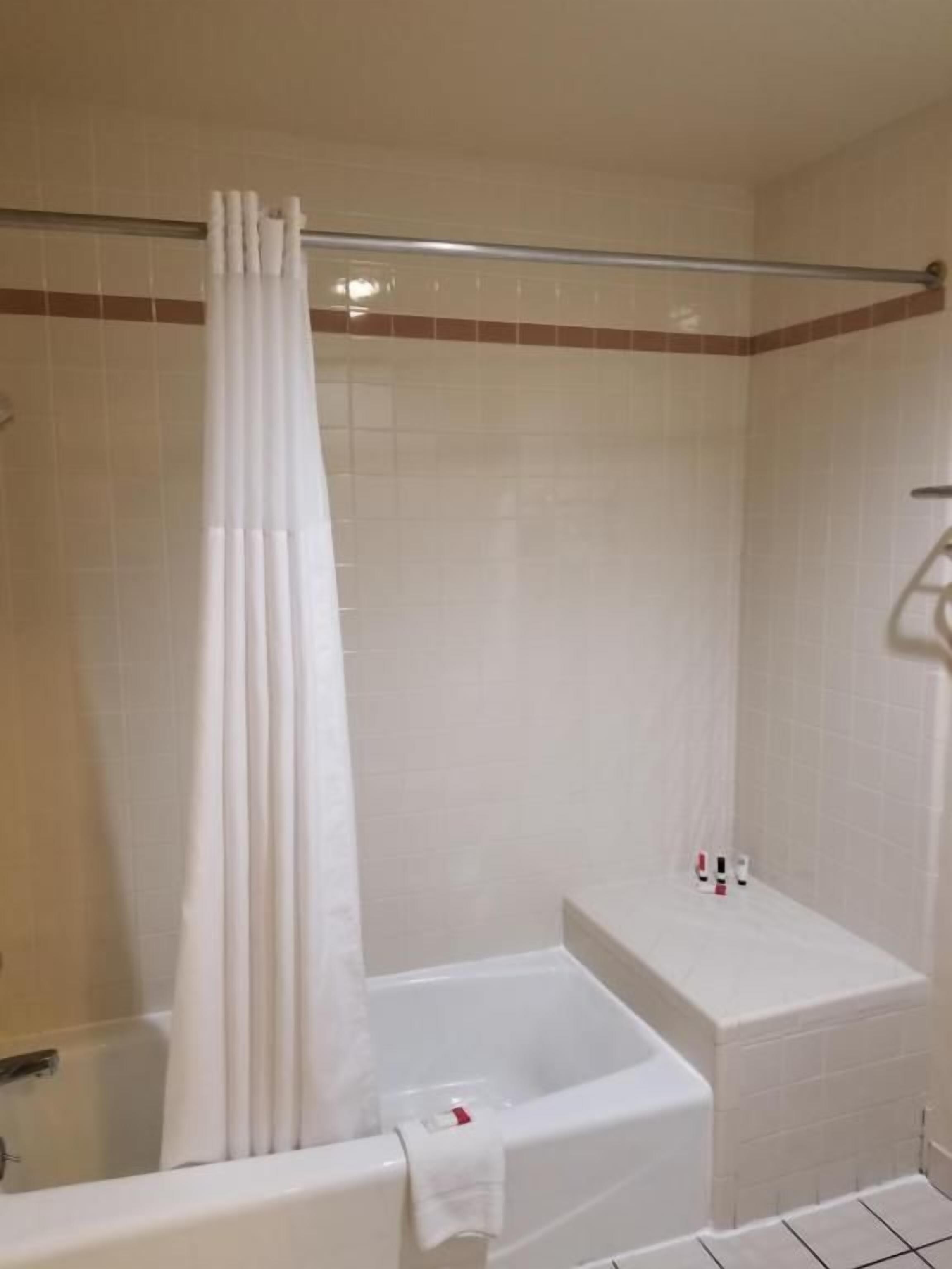A bathroom with a bathtub, a shower curtain, and a small shelf with toiletries.