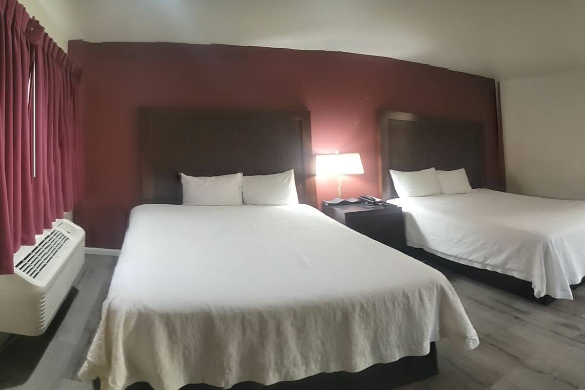 A hotel room with two beds, a desk, a chair, a TV, and a heater.