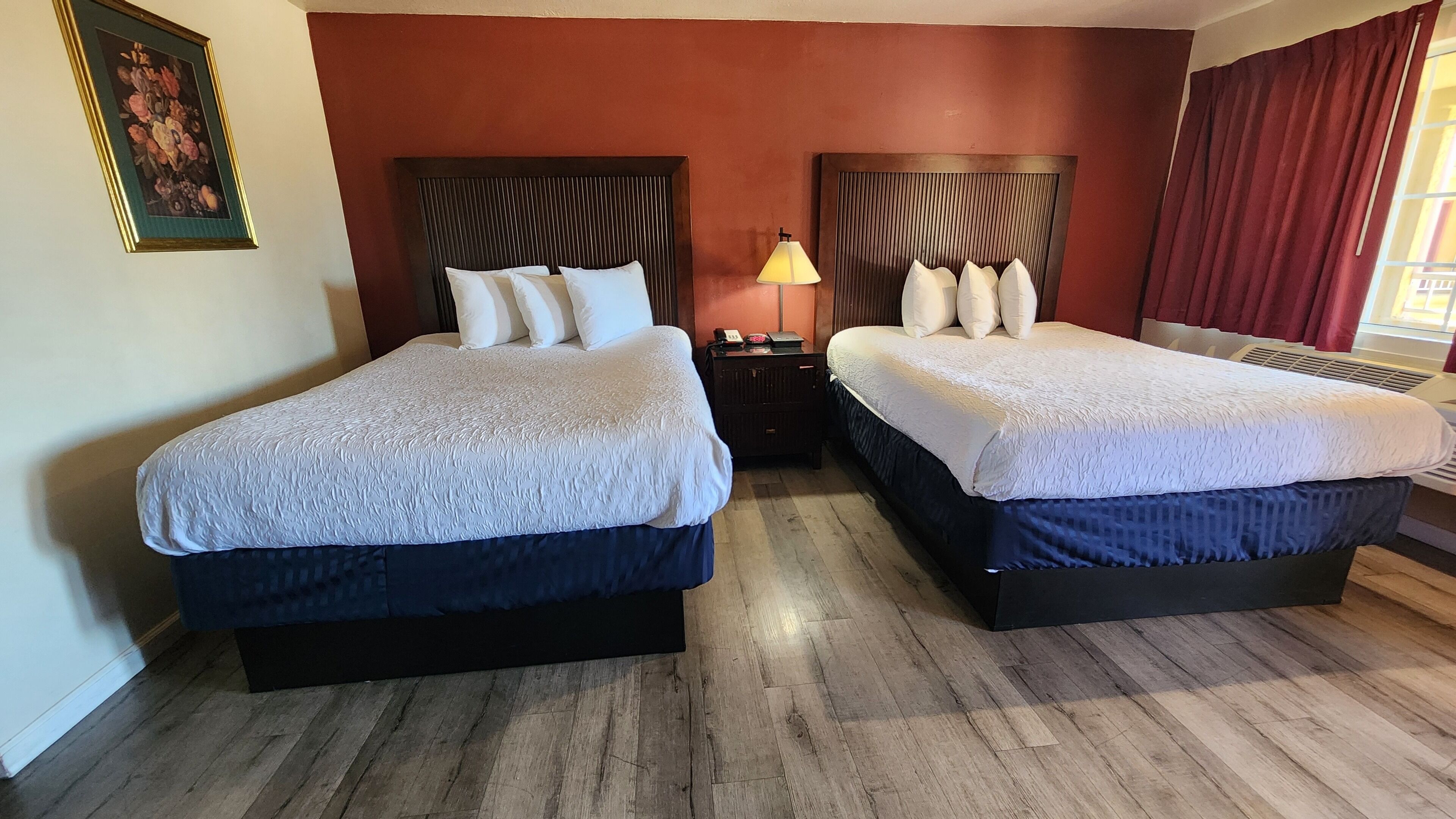 Habitación de hotel con dos camas, piso de madera y pared roja.