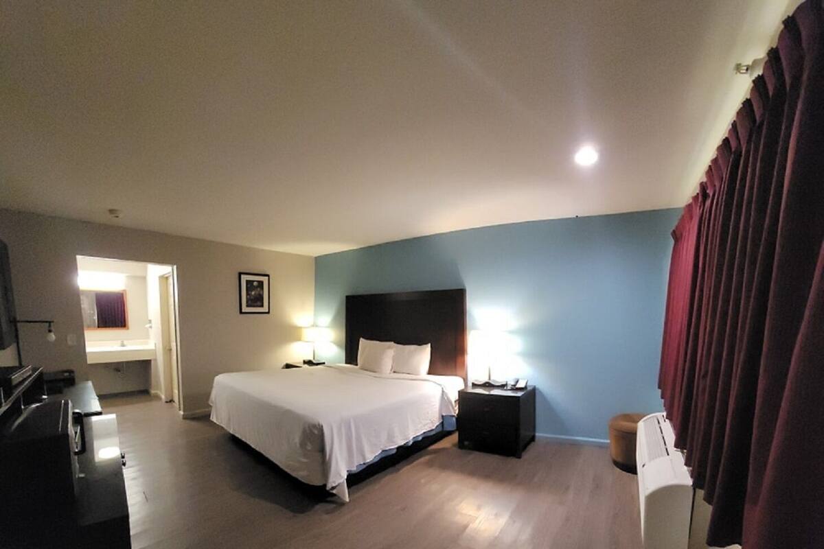 A hotel room with a large bed, bedside tables with lamps, a desk, a chair, and a window with curtains.