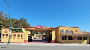 A Mission Inn & Suites with a red roof and yellow walls, featuring a central entrance and multiple windows. - Mission Inn and Suites (Hayward)