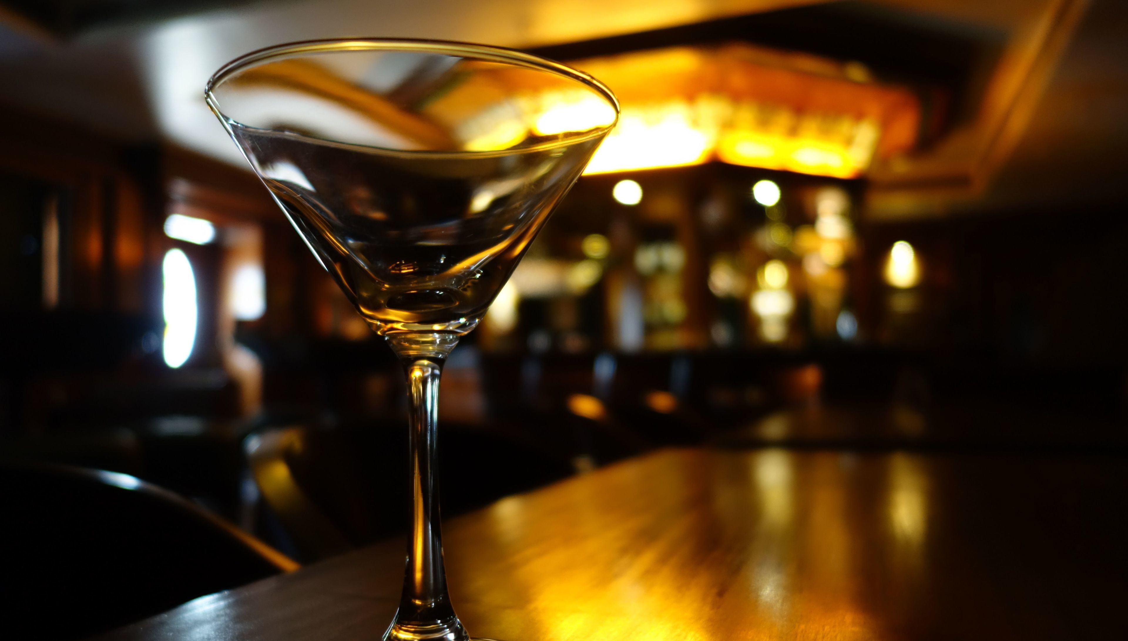 A martini glass on a bar counter with a blurred background of a bar area.