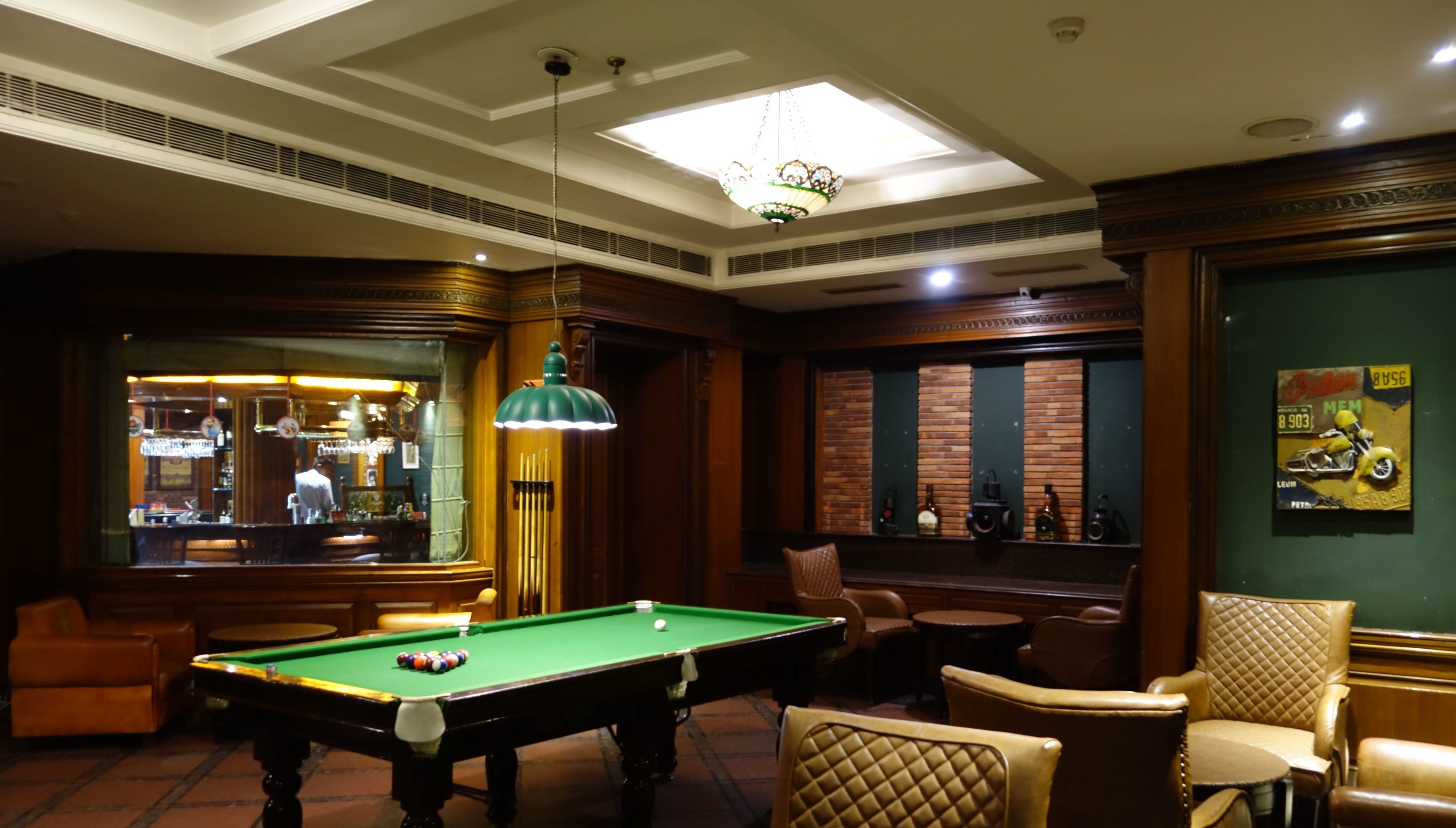 A billiards room with a pool table, leather chairs, a bar area, and a decorative wall with a motorcycle poster.