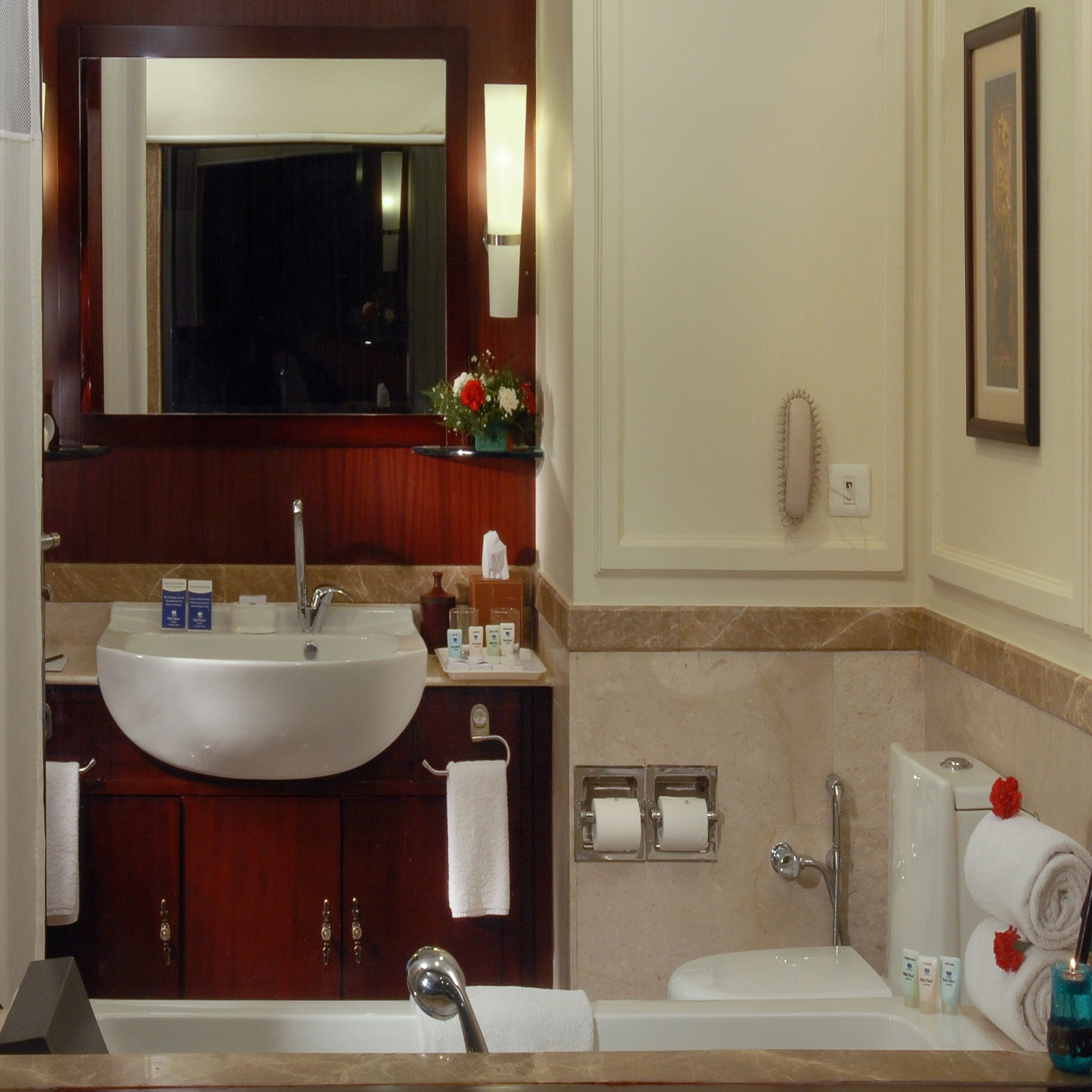 A bathroom with a large sink, mirror, and bathtub. There are toiletries on the counter and a towel rack.