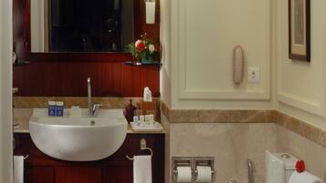 A bathroom with a large sink, mirror, and bathtub. There are toiletries on the counter and a towel rack.