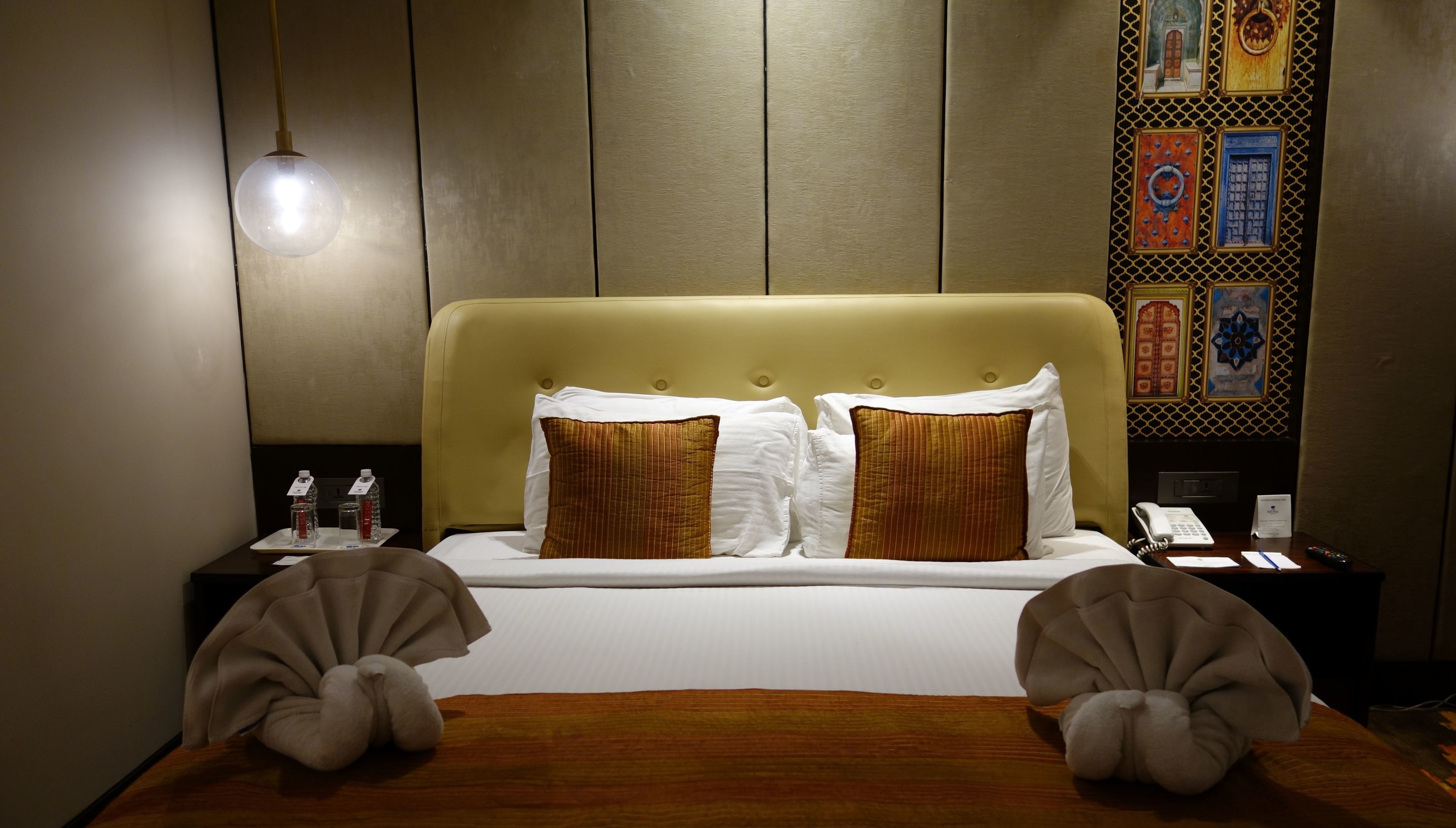 Una habitación de hotel con una cama, dos mesitas de noche, una lámpara y un adorno en la pared.