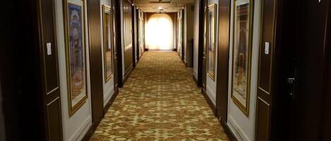 Un pasillo de hotel con alfombra estampada, puertas a ambos lados y cuadros enmarcados en las paredes.