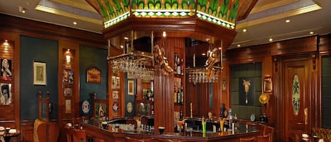 Zona de bar con mostradores de madera, sillas tapizadas en verde y techo decorativo con patrones verdes y dorados.