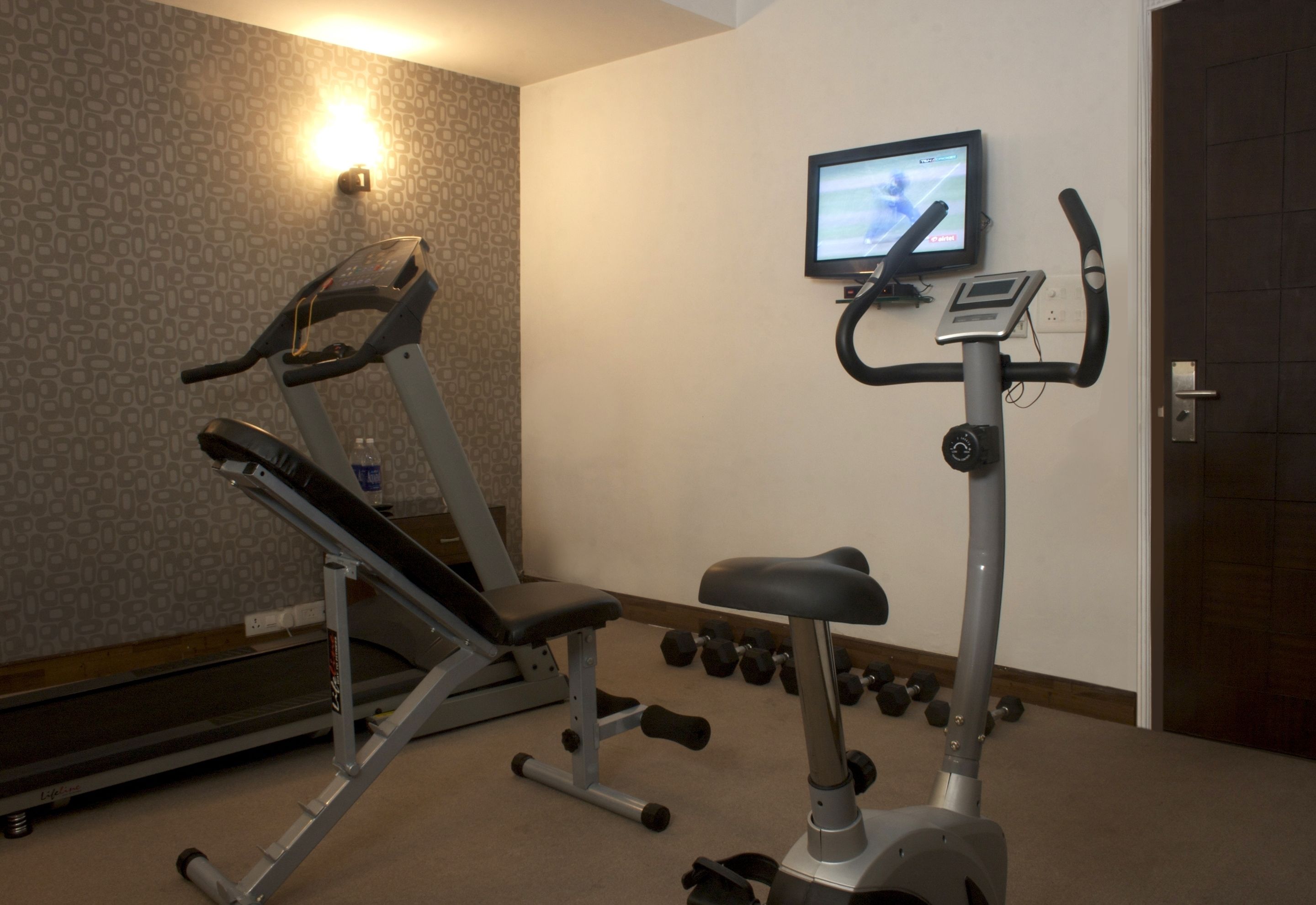 Een fitnessruimte met cardioapparatuur, een televisie en gewichten.