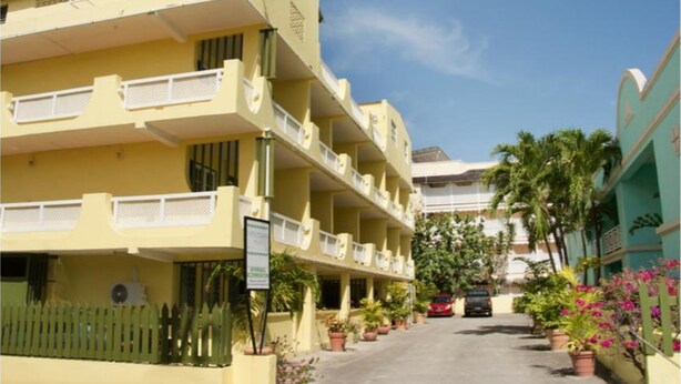 A multi-story yellow building with balconies, a gated entrance, and potted plants along the street.