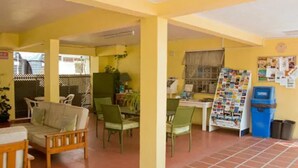 A spacious indoor area with a dining table, chairs, a sofa, and a bulletin board. - Meridian Inn (St. Lawrence Gap)