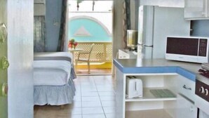 A compact room with a bed, kitchenette, and a ceiling fan.
