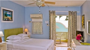 A bedroom with a bed, a nightstand, a desk, a chair, a ceiling fan, and a window with curtains. - Meridian Inn (St. Lawrence Gap)