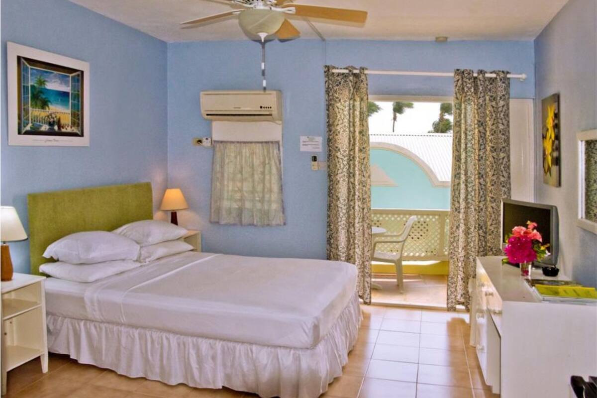A bedroom with a bed, a nightstand, a desk, a chair, a ceiling fan, and a window with curtains.