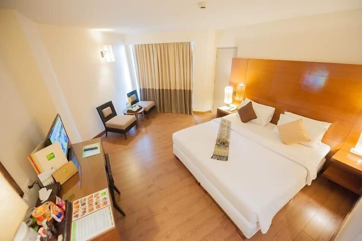 A hotel room with a large bed, a desk with a computer, a chair, and a small table.