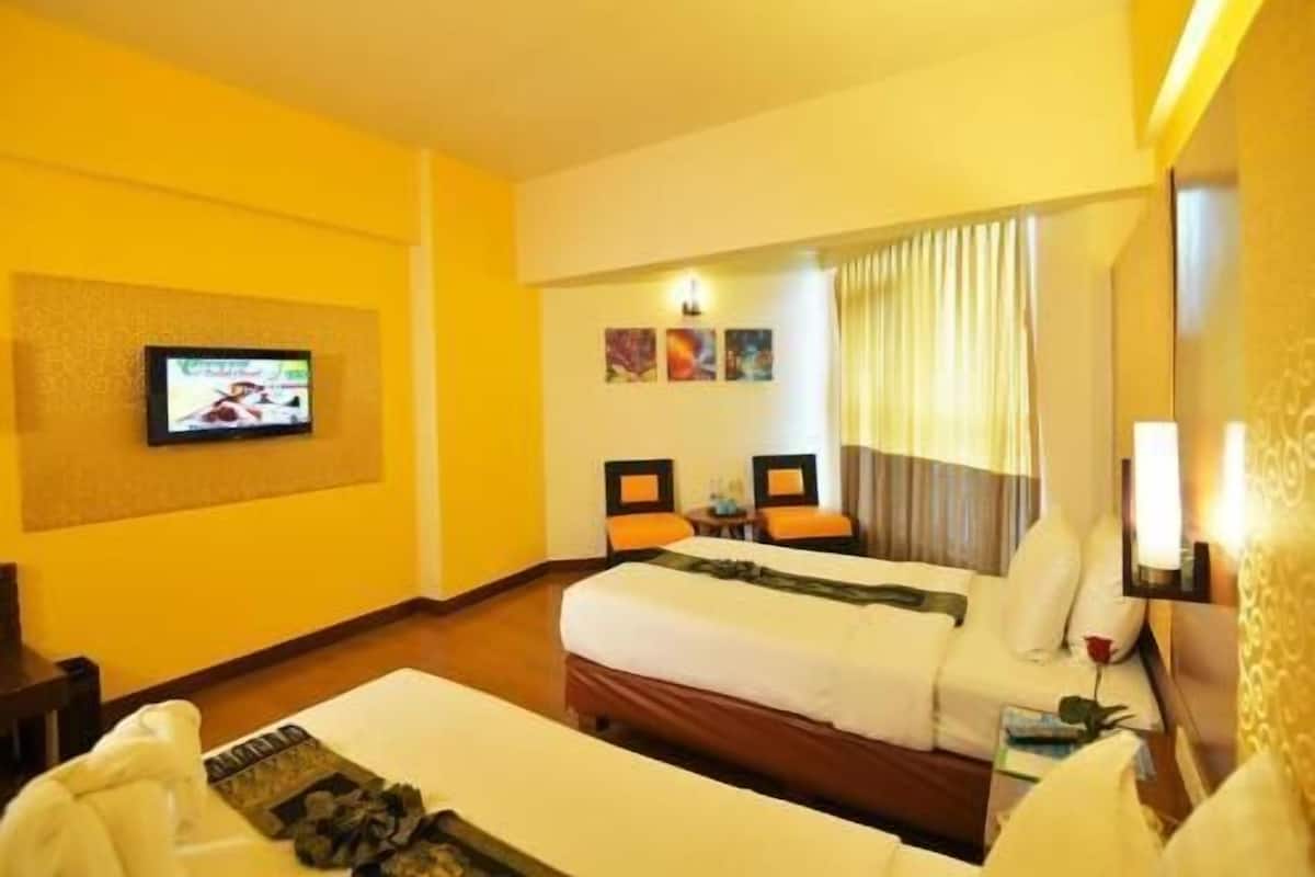 A hotel room with two beds, a television, a desk, and a window with curtains.