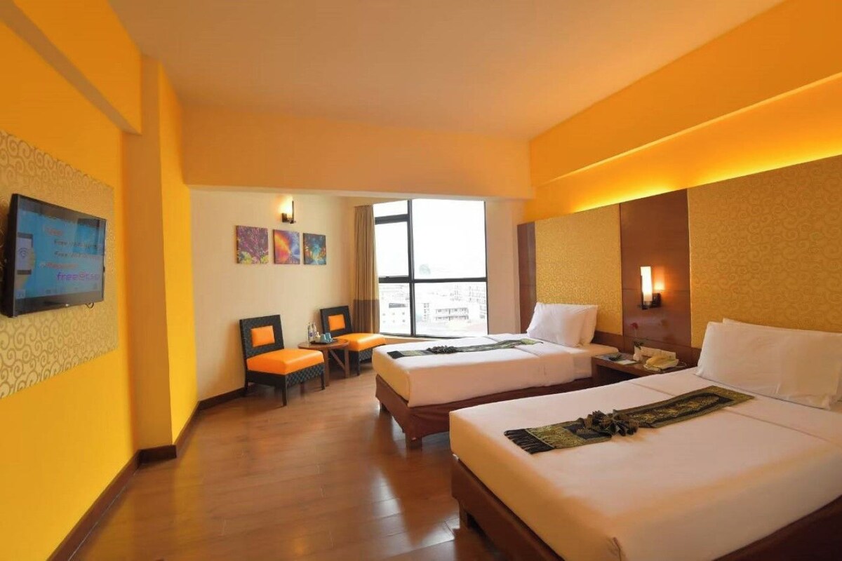 A hotel room with two beds, a desk, and a chair. There is a window providing a view outside.