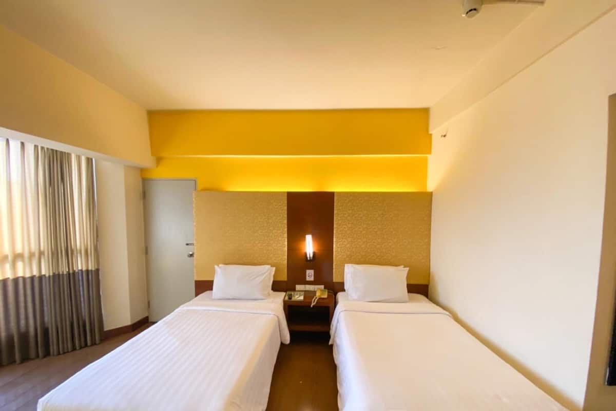 A hotel room with two beds, a nightstand, a lamp, and a door.
