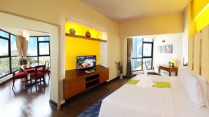 A hotel room with a large bed, a TV on a wooden stand, a dining area with red chairs, and a view through large windows. - The Seasons Pattaya (Pattaya)