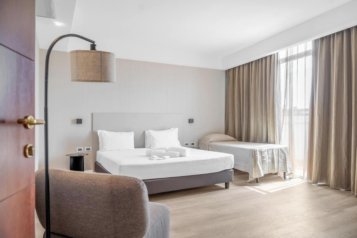 Ein modernes Hotelzimmer mit einem großen Bett, einem Nachttisch, einem Sessel und einem Fenster mit Vorhängen.