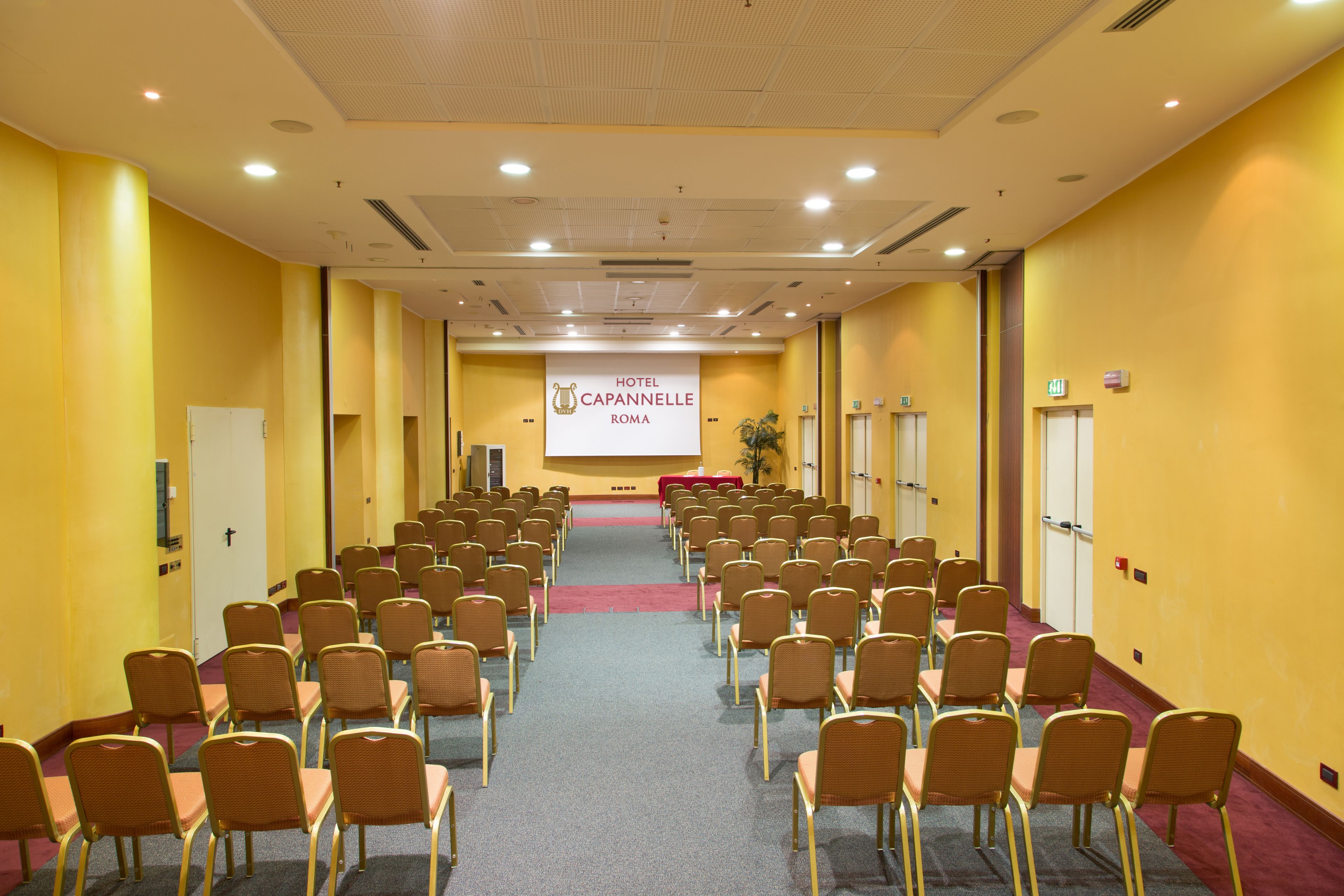 A hotel conference room with rows of chairs, a podium, and a projection screen displaying the hotel name.