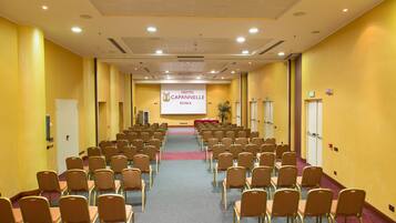 A hotel conference room with rows of chairs, a podium, and a projection screen displaying the hotel name.