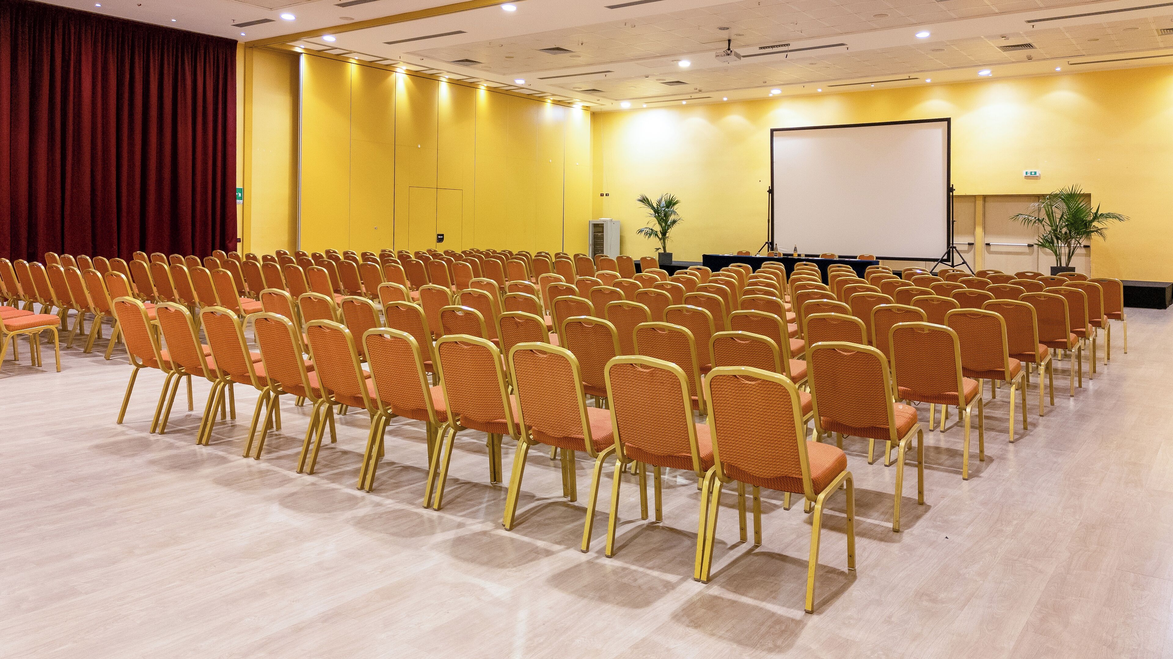 A conference room with rows of chairs, a projection screen, and a stage.