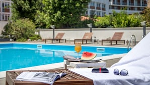 En avslappnad plats vid poolen med ett glas apelsinjuice, en bit vattenmelon och solglasögon på en handduk.