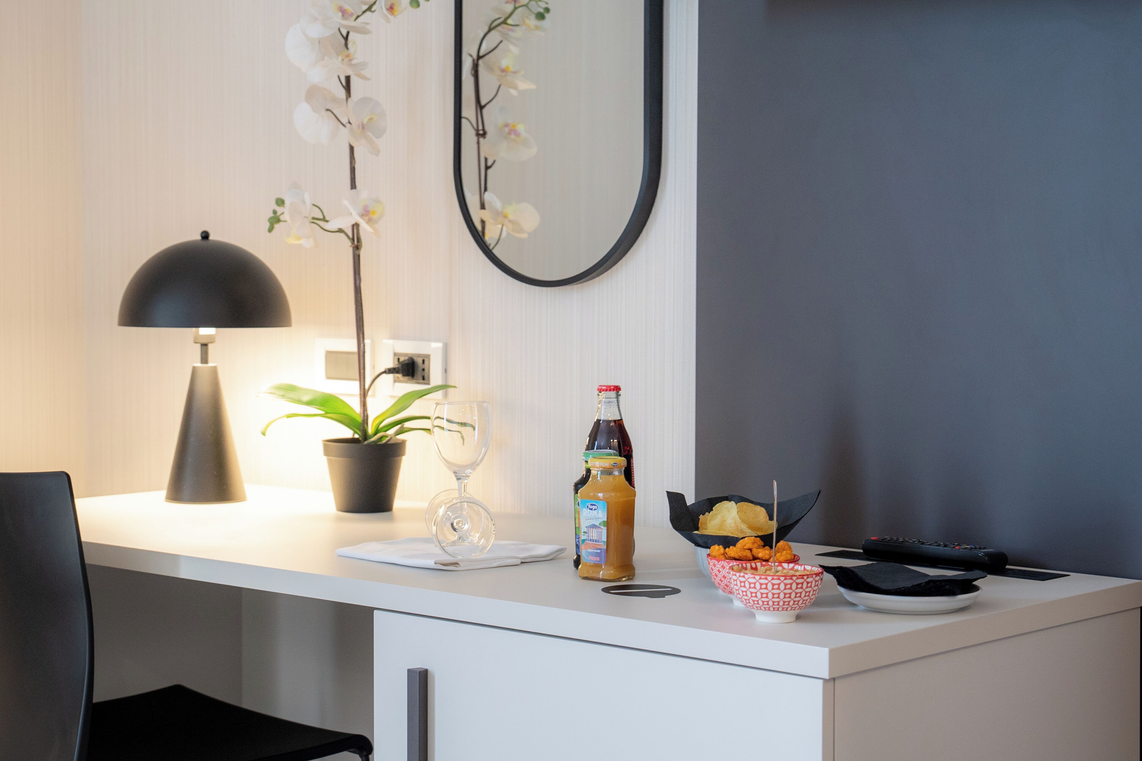 Una cucina moderna con un piano di lavoro bianco, una pianta in vaso, un bicchiere da vino, una bottiglia di salsa e una ciotola di snack.