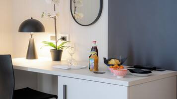 A modern kitchen with a white countertop, a potted plant, a wine glass, a bottle of sauce, and a bowl of snacks.