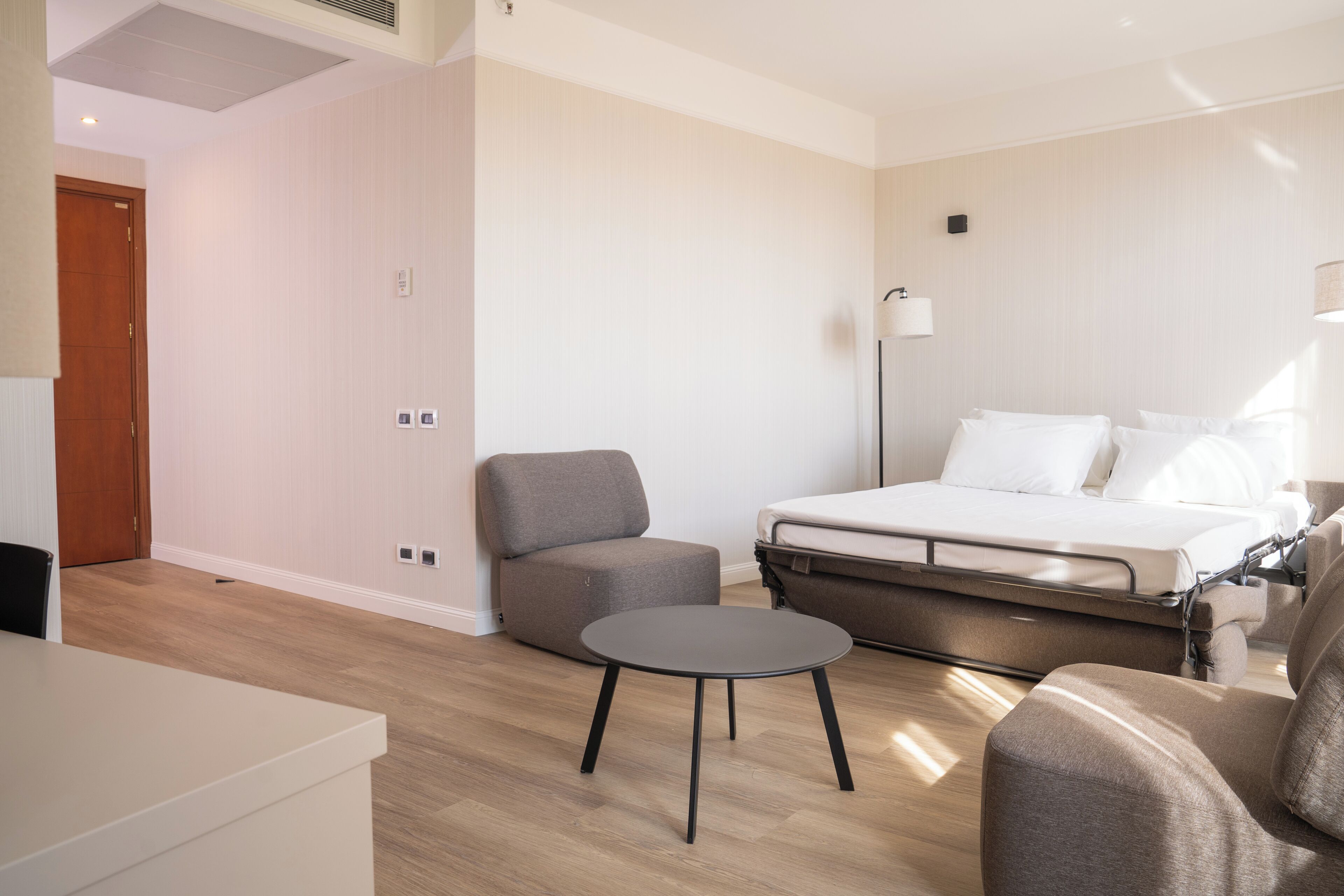 Una habitación de hotel moderna con una cama, una pequeña mesa redonda, un sofá y una silla.