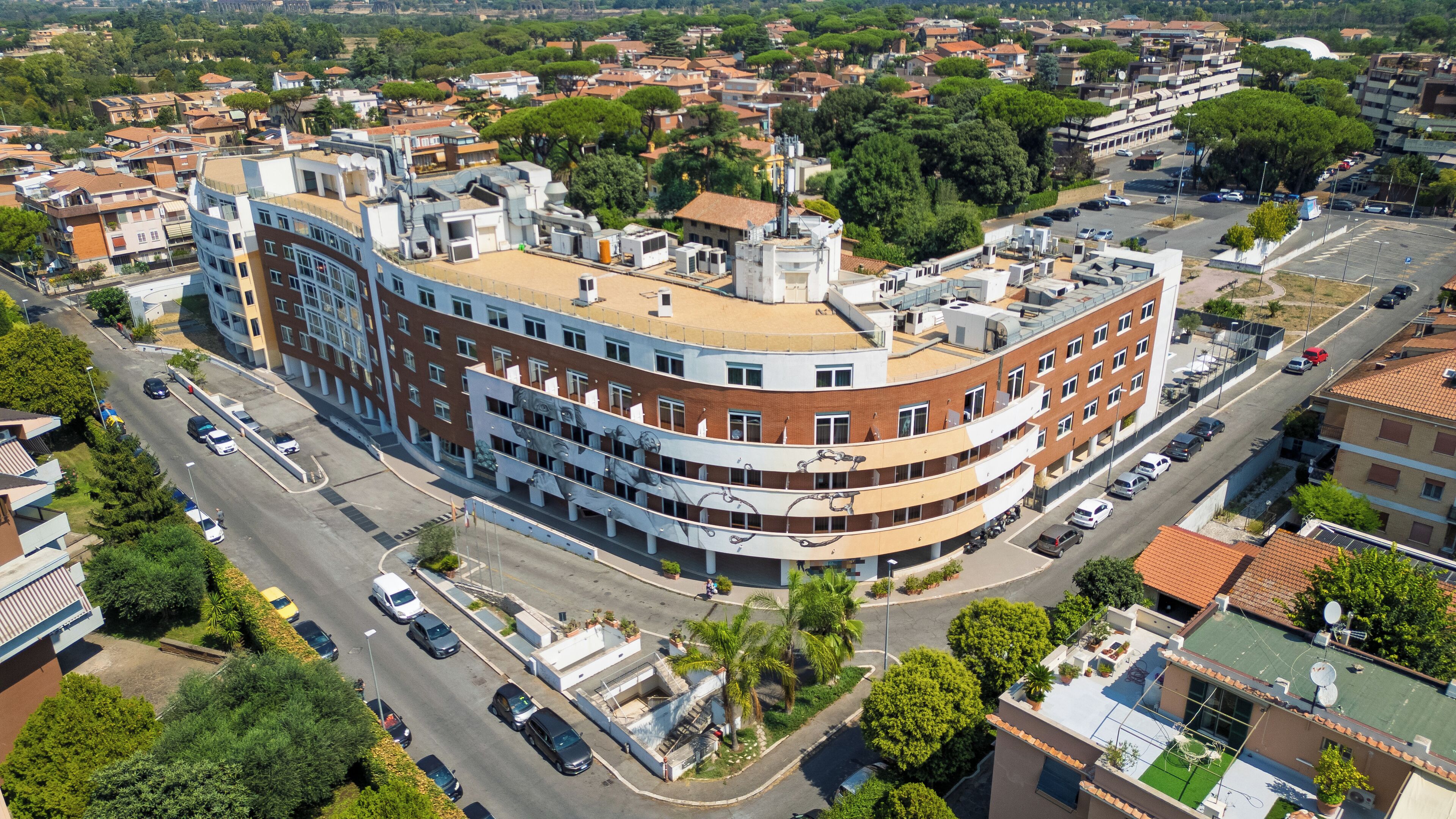 Un edificio a più piani con una facciata curva, un parcheggio e vegetazione circostante.