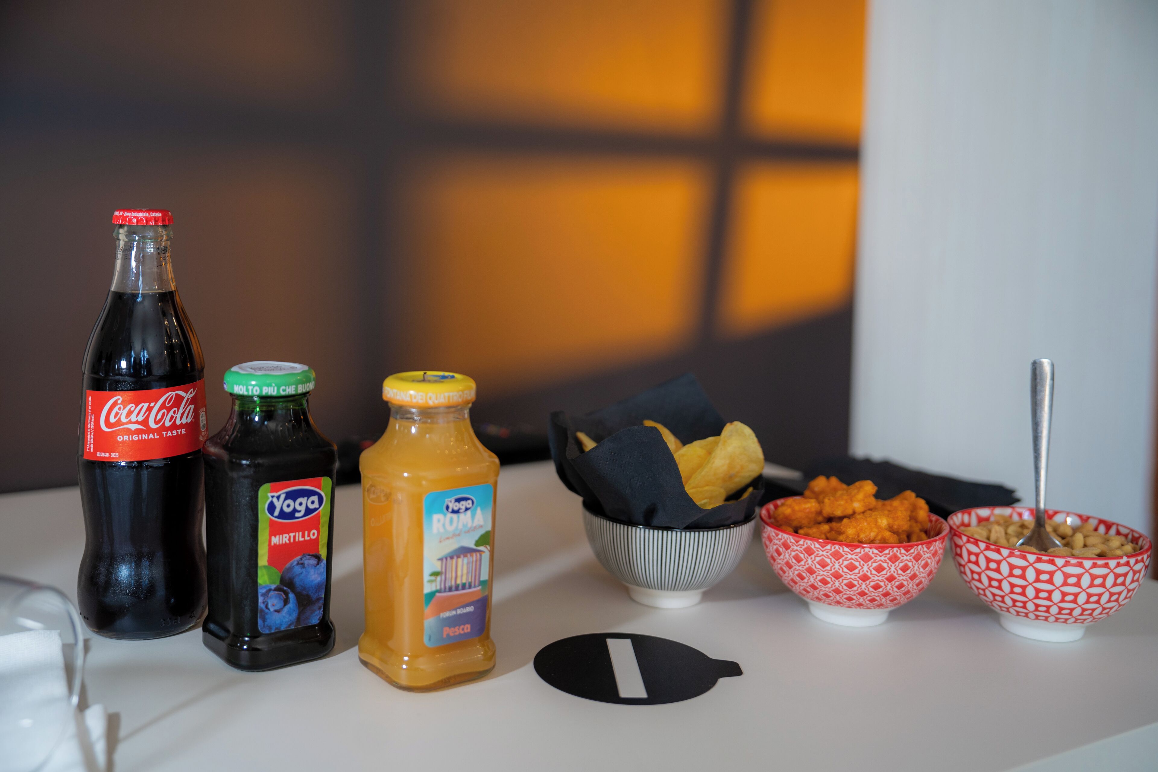 Una mesa con diferentes alimentos y bebidas, incluyendo Coca-Cola, una botella de jugo y tazones de bocadillos.