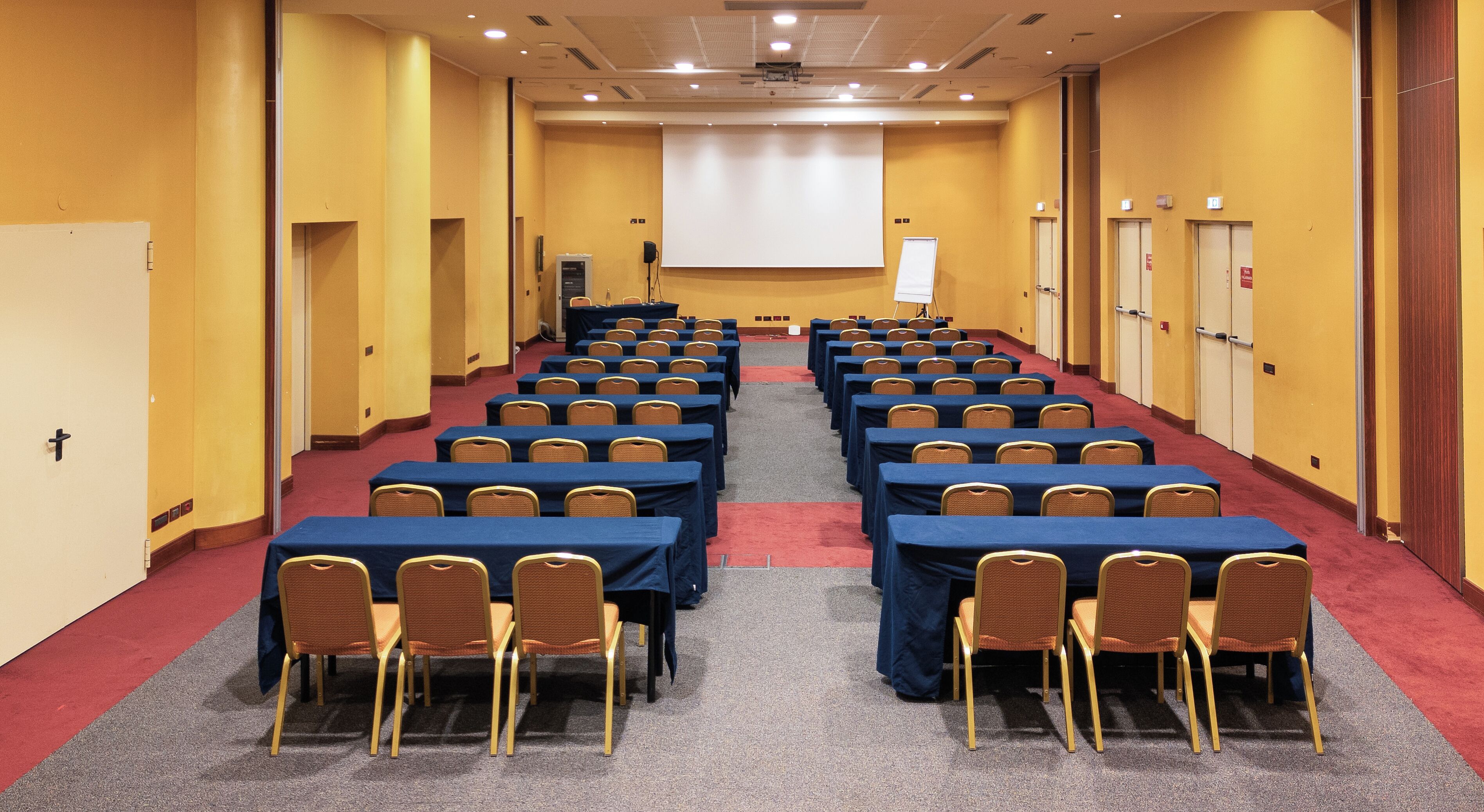 Ein Konferenzraum mit Tischen und Stühlen, einer Projektionsleinwand und einer Whiteboard-Tafel.