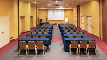 Ein Konferenzraum mit Tischen und Stühlen, einer Projektionsleinwand und einer Whiteboard-Tafel.