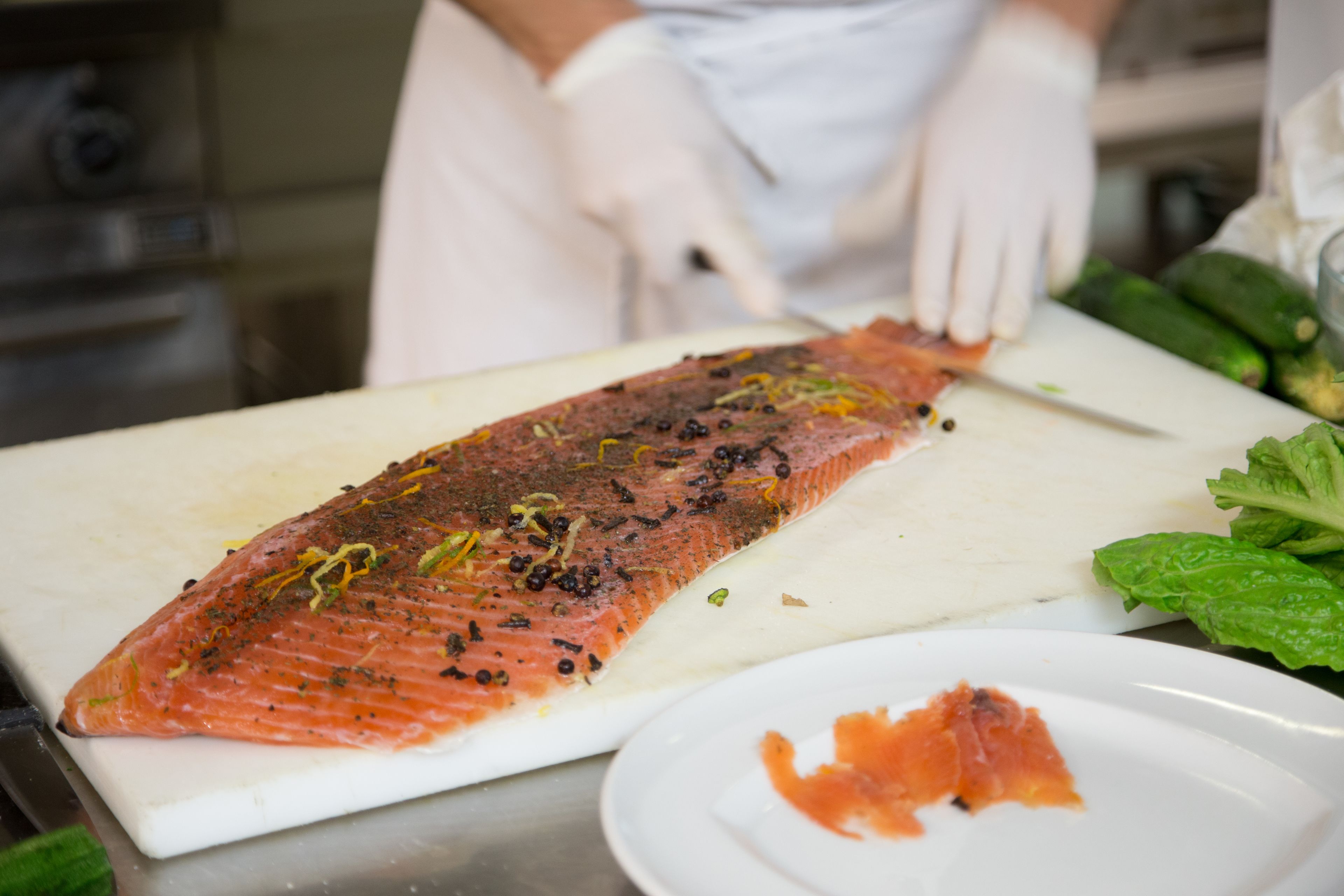 A chef preparing salmon on a cutting board with a knife.