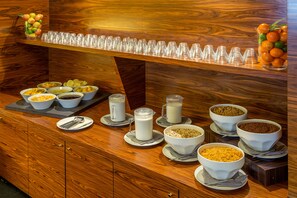 En frukostbuffé med ett varierat utbud av mat och dryck, inklusive skålar med flingor, mjölk och frukt.