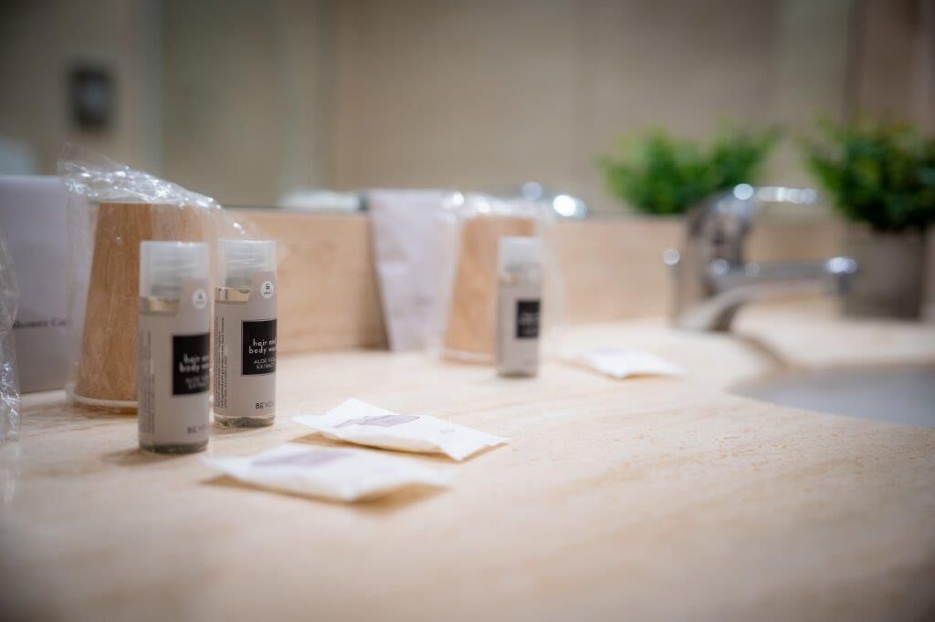 A bathroom counter with various toiletries and a plant in the background.