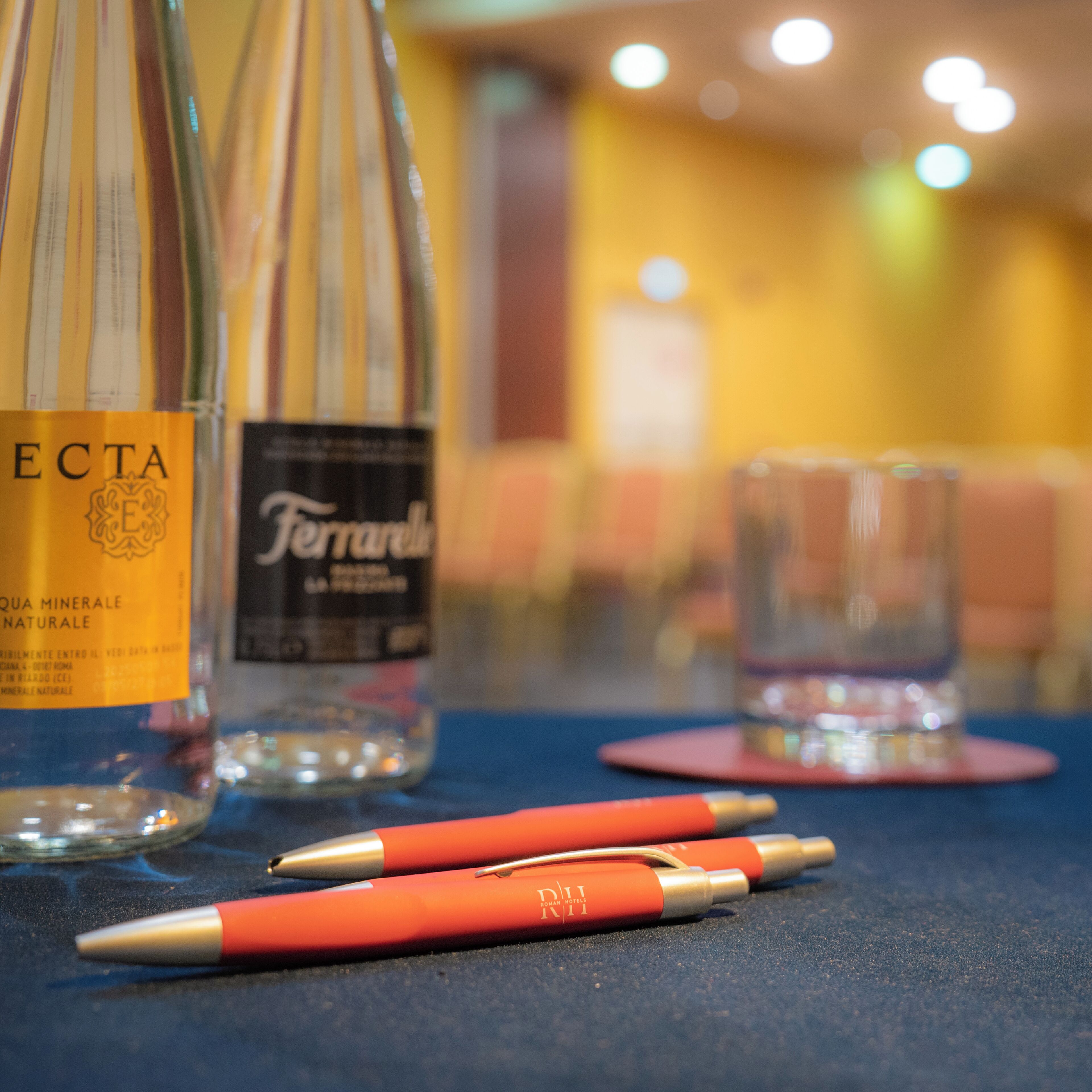 A table with two bottles of water, a glass, and two pens.